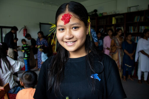 A junior girl at Olgapuri smiles at the camera with a tika on her forehead.